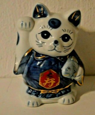 Blue And White Lucky Cat With Right Paw Raised And Holding A Fish